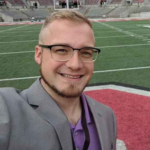 Jared Starner smiling in a gray blazer on the field at Ohio Stadium.